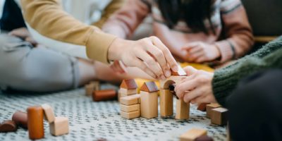 Nahaufnahme von fröhlichen asiatischen Eltern, die im Wohnzimmer auf dem Boden sitzen und Spaß haben und mit ihrer Tochter zusammen Holzbausteine spielen?