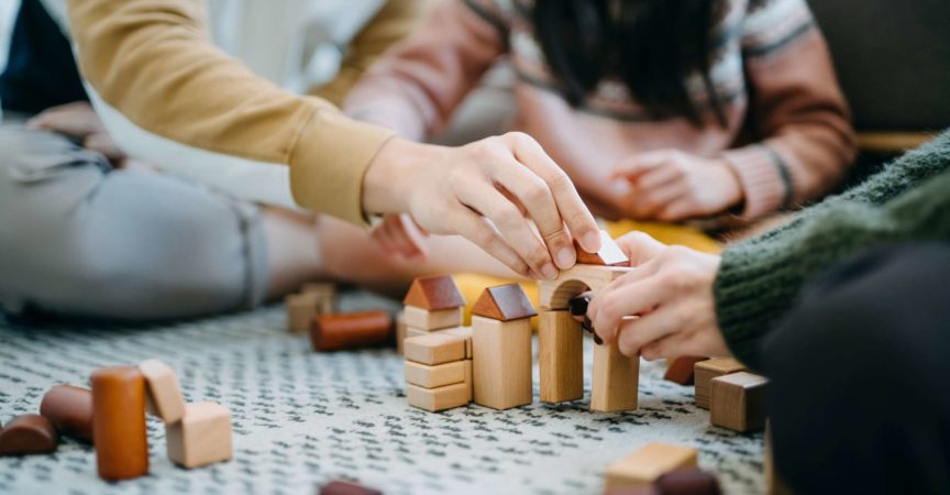 Nahaufnahme von fröhlichen asiatischen Eltern, die im Wohnzimmer auf dem Boden sitzen und Spaß haben und mit ihrer Tochter zusammen Holzbausteine spielen?