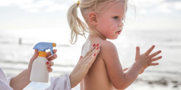 Mother applying sunscreen protection lotion on cute little toddler girl