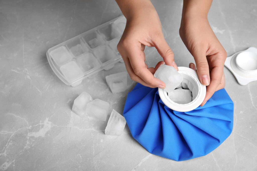 Woman putting ice cubes into pack at marble table, closeup