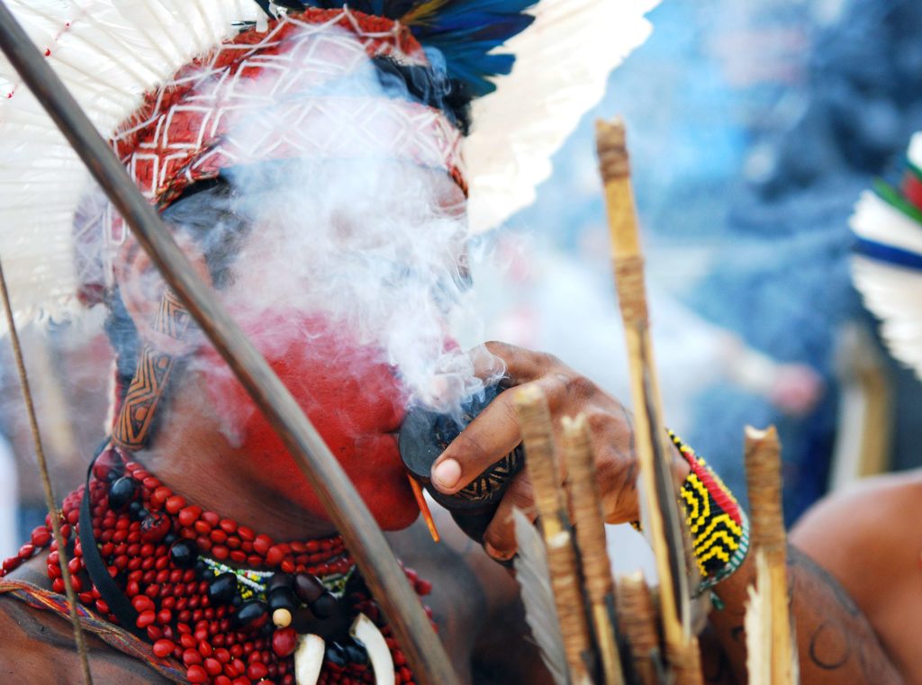 Indigenous face painted man with smoke around his head.