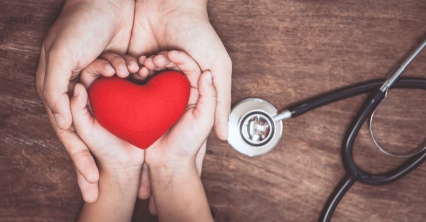Rotes Herz auf Frauen- und Kinderhänden und mit Stethoskop des Doktors auf hölzernem Hintergrund. Medizinisches Konzept des Gesundheitswesens