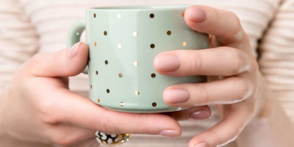 Woman with groomed hands with nude beige pink nail design holding cup. Manicure, fashion and beauty salon concept