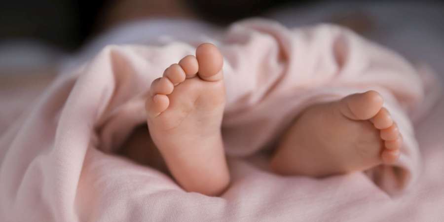 Winzige Babyfüße bedeckt mit einer weichen pastellfarbenen Pfirsichdecke, entzückende kleine Zehen