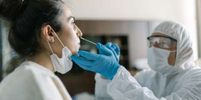 Arzt in Arbeitsschutzkleidung, der einen Nasenabstrichtest von einer jungen Frau durchführt