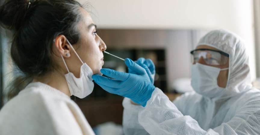 Arzt in Arbeitsschutzkleidung, der einen Nasenabstrichtest von einer jungen Frau durchführt