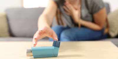 Mädchen mit Asthmaanfall, der einen Inhalator auf einer Couch im Wohnzimmer zu Hause erreicht