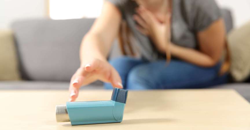 Mädchen mit Asthmaanfall, der einen Inhalator auf einer Couch im Wohnzimmer zu Hause erreicht