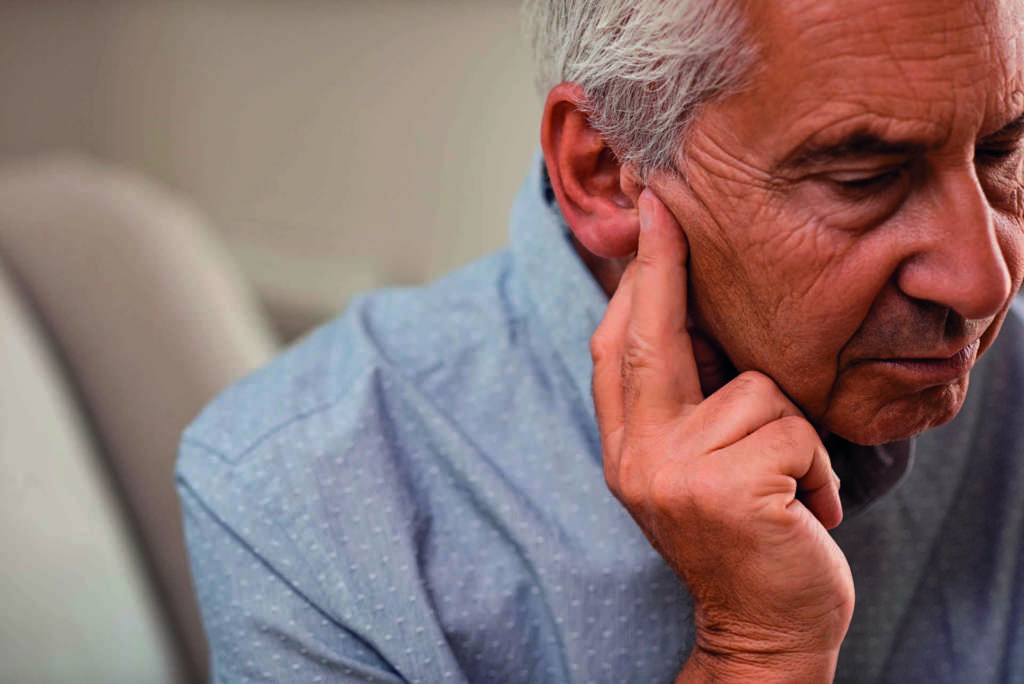 Seitenansicht eines älteren Mannes mit dem Symptom von Hörverlust. Reifer Mann sitzt auf der Couch mit den Fingern in der Nähe des Ohrs und leidet unter Schmerzen.