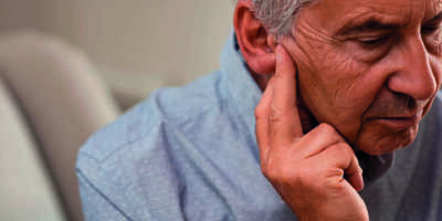 Seitenansicht eines älteren Mannes mit dem Symptom von Hörverlust. Reifer Mann sitzt auf der Couch mit den Fingern in der Nähe des Ohrs und leidet unter Schmerzen.
