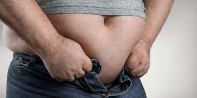 Fettleibigkeitskonzept, Nahaufnahme eines übergewichtigen Mannes, der versucht, zu kleine Jeans mit Kopierraum zu tragen