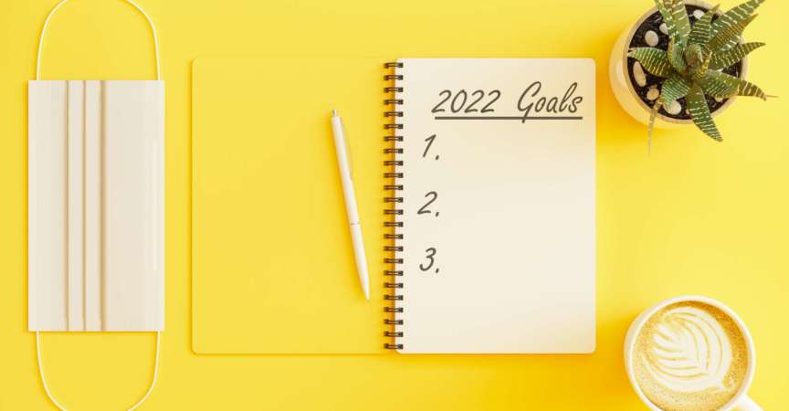 2022 Neujahrsziele Konzept. Draufsicht auf Schutzmaske, Topfpflanze und Kaffeetasse auf gelbem Hintergrund