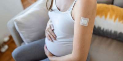 Schwangere Frau zeigt geimpften Arm mit Pflaster nach der Injektion des Coronavirus Impfstoff