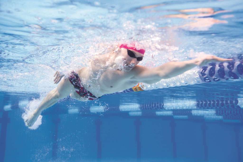 Underwated Foto eines jungen muskulösen Mannes, der Kraulschwimmen durch das olympische Schwimmbecken schwimmt.