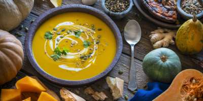 Herbstliche Kürbissuppe und Zutaten auf rustikalem Holztisch