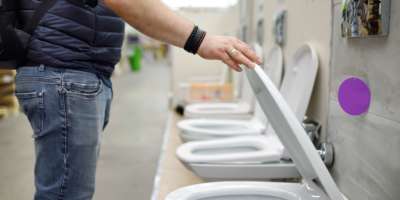 Mann wählt eine neue Toilette im Baumarkt. Vielzahl von Sanitärkeramik im Baumarkt. Heimwerkermarkt