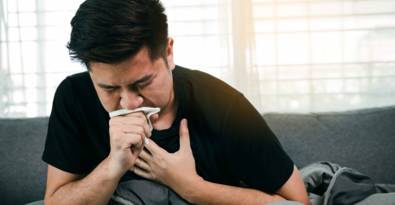 Asiaten erkranken oder erkranken an Bronchitis beim Husten, indem sie sich den Mund mit Seidenpapier zudecken, wenn er zu Hause auf dem Sofa sitzt.