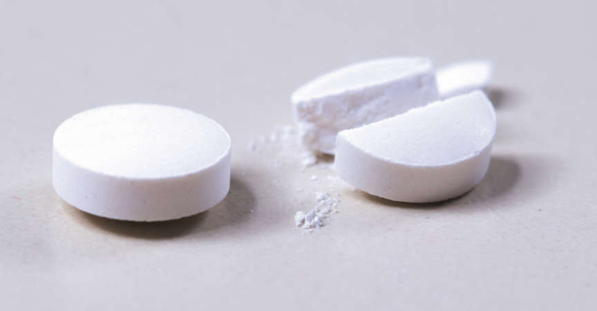 Two pills crushed and whole on white background