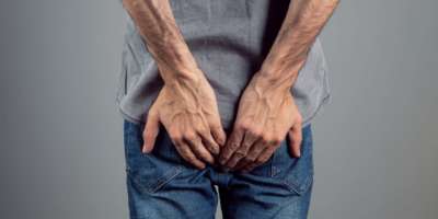 Mann mit Hämorrhoiden, der Arsch auf grauem Hintergrund hält