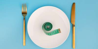 weiße runde Platte und goldene Gabel und Messer mit grünem Maßband auf blauem Hintergrund, Gewichtsverlustkonzept, flache Lage.