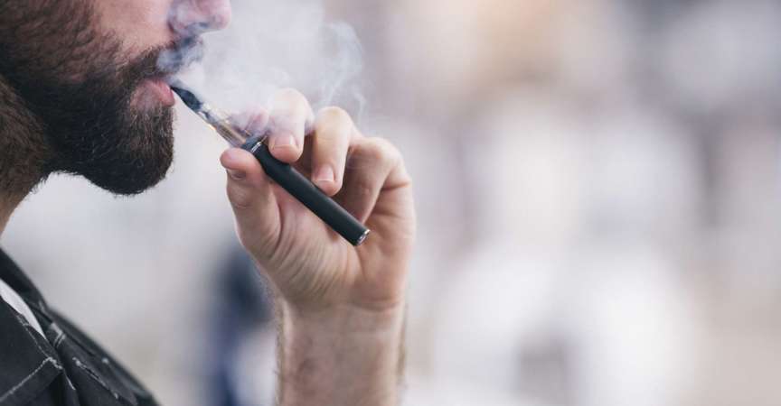 Junger männlicher Arbeiter, der elektronische Zigarette raucht