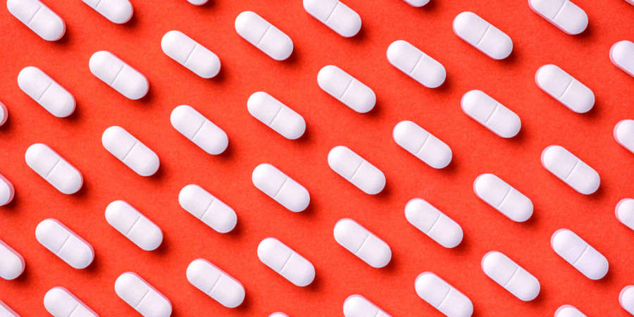 Orange und roter Medizinhintergrund mit weißen Pillen und Tablette, Makro.