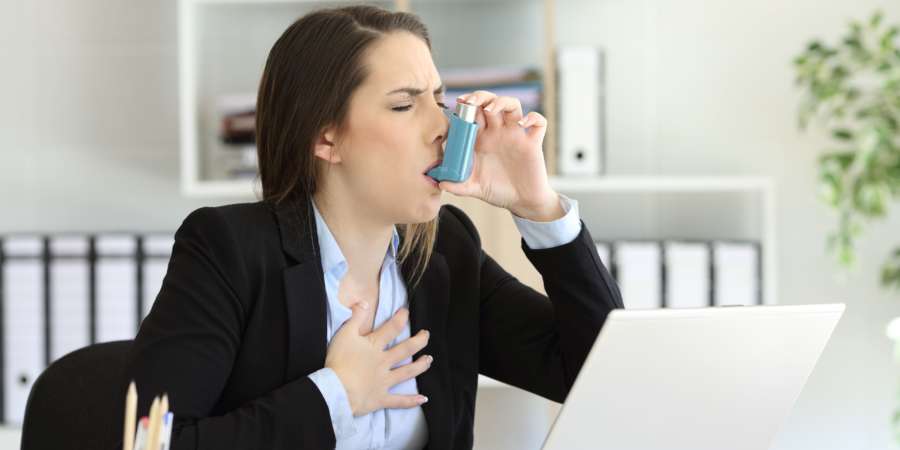 Asmathische Führungskraft mit einem Asthmaanfall, der im Büro mit einem Inhalator inhaliert