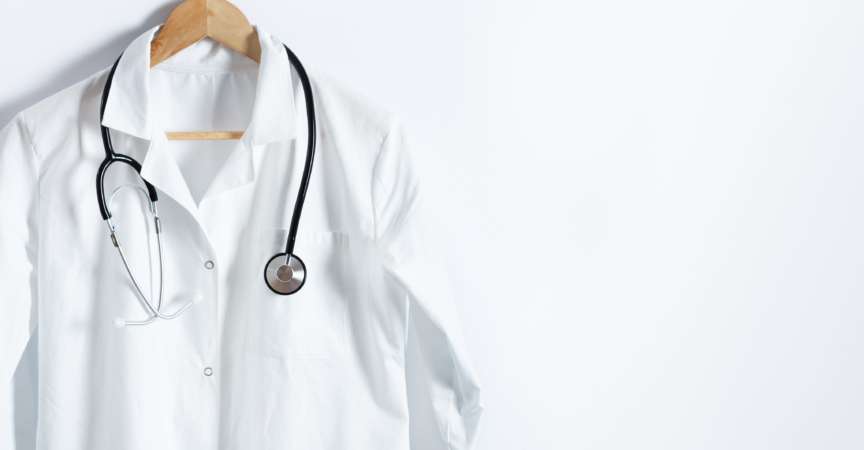 Weißer Kittel des Doktors mit Stethoskop auf Aufhänger über weißem Hintergrund mit Kopienraum. Gesundheitswesen und medizinisches Konzept.