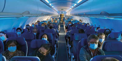 Gang eines vollen Flugzeuges mit Passagieren, die eine Gesichtsmaske tragen