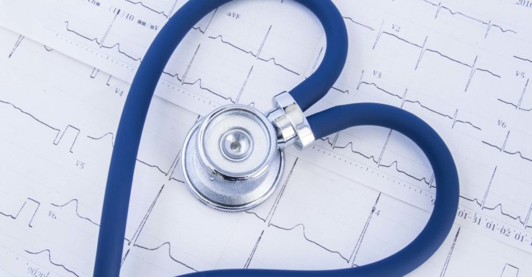 Herzförmiges Stethoskop vor dem Hintergrund des Elektrokardiogramms (ekg). Kopf oder Bruststück und flexibler Schlauch aus blauem Stethoskop, gefaltet in Herzform, die auf gedrucktem Elektrokardiogramm liegt
