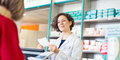 Glückliche Apothekerin, die Frauen beim Kauf von Medikamenten in der Apotheke hilft