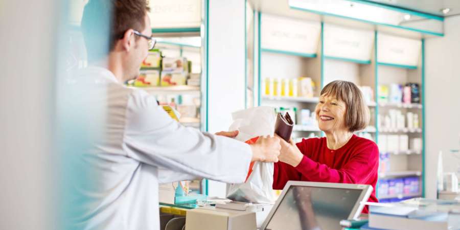 Männlicher Apotheker gibt älteren Kunden in einer Apotheke verschreibungspflichtige Medikamente