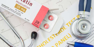 Offene Verpackung mit Medikamententabletten, auf der „Statin Medication“ steht, liegt in der Nähe von Stethoskop, Ergebnisanalyse zu Cholesterin (Lipidpanel) und EKG