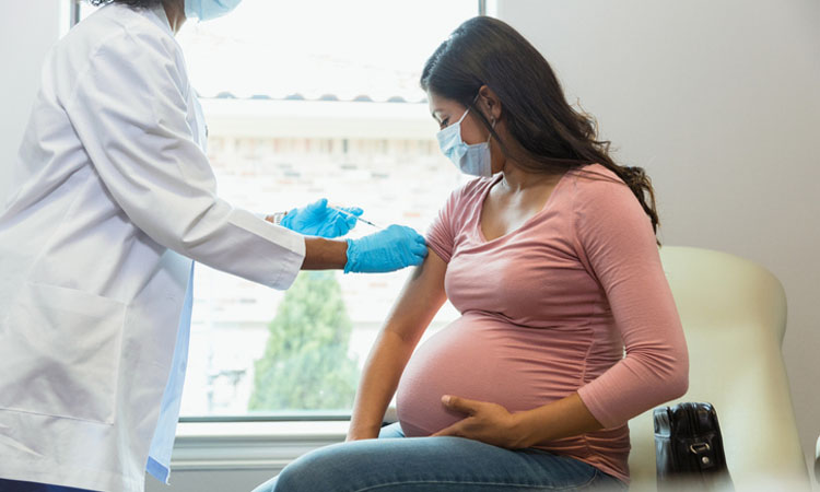 Eine schwangere Frau mit Schutzmaske beobachtet, wie die Ärztin eine Impfung verabreicht.