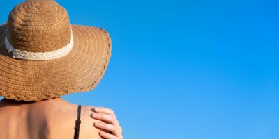 Sommerferienstimmung: Frau mit Strandhut, bedeckt mit Sand auf hellblauem Hintergrund.