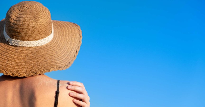 Sommerferienstimmung: Frau mit Strandhut, bedeckt mit Sand auf hellblauem Hintergrund.