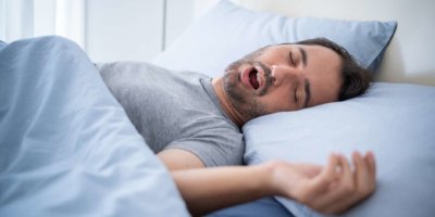 Mann schnarcht laut in seinem Bett, während er schläft