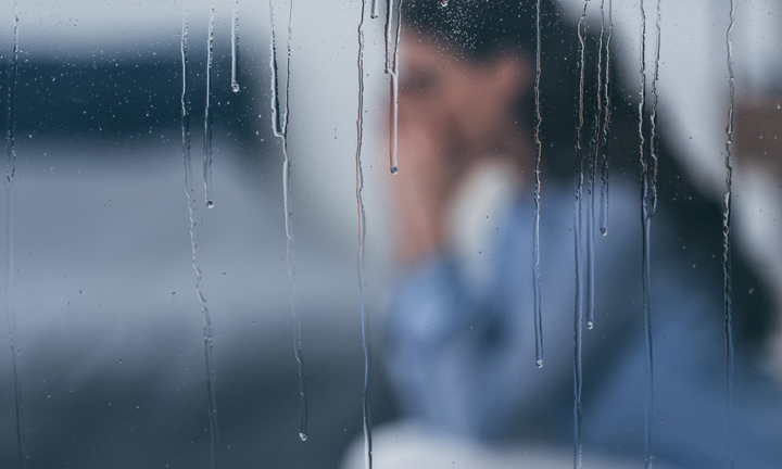 Deprimierte Frau sitzt auf Sofa hinter verregneter Glasscheibe