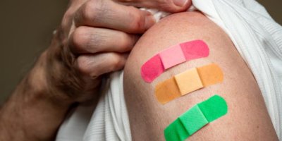 Alte Person zieht seinen Ärmel hoch und zeigt drei farbige Pflaster von Impfungen auf dem Oberarm