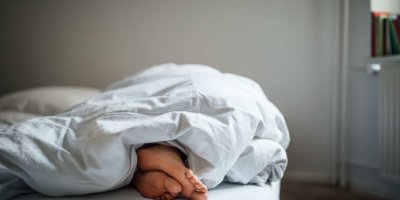 Niedriger Abschnitt der jungen Frau, die im Bett schläft. Die nackten Füße der Frau unter der Decke im Schlafzimmer. Sie ruht sich zu Hause aus.