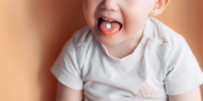 Selektiver Fokus auf eine weiße Pille auf der Zunge eines kleinen Kleinkindes.
