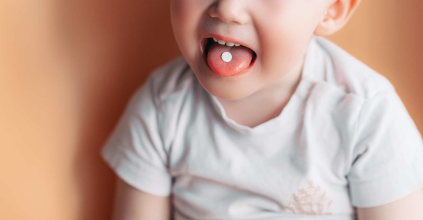 Selektiver Fokus auf eine weiße Pille auf der Zunge eines kleinen Kleinkindes.