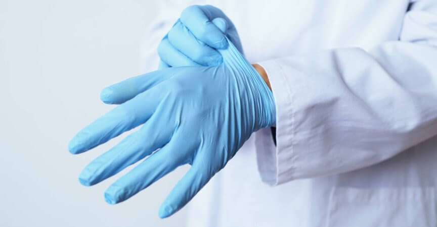 Nahaufnahme eines kaukasischen Arztes, der einen weißen Kittel trägt und ein Paar blaue OP-Handschuhe anzieht