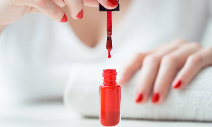 Close-up of red nail polish drop  wih woman nails on backbround