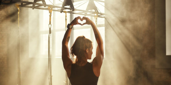 Trainierte Frau im Fitnessstudio hält ihre Hände in die Höhe und formt ein Herz