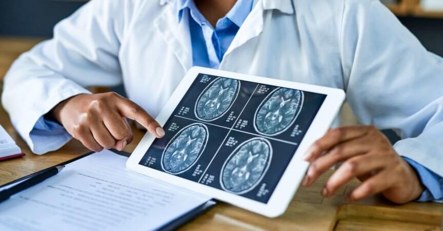 Aufnahme einer Ärztin, die während einer Beratung in ihrer Praxis ein digitales Tablet verwendet, um einen Gehirnscan zu besprechen