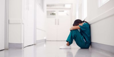 Gestresste und überarbeitete Ärztin, die Scrubs trägt, sitzt auf dem Boden im Krankenhauskorridor