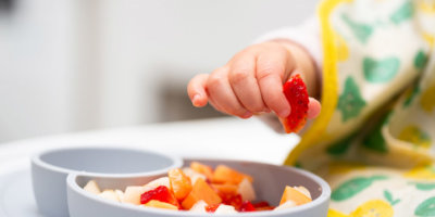Macro Close up of Baby Hand with a Piece of Fruits Sitting in Child's Chair Kid Eating Healthy Food