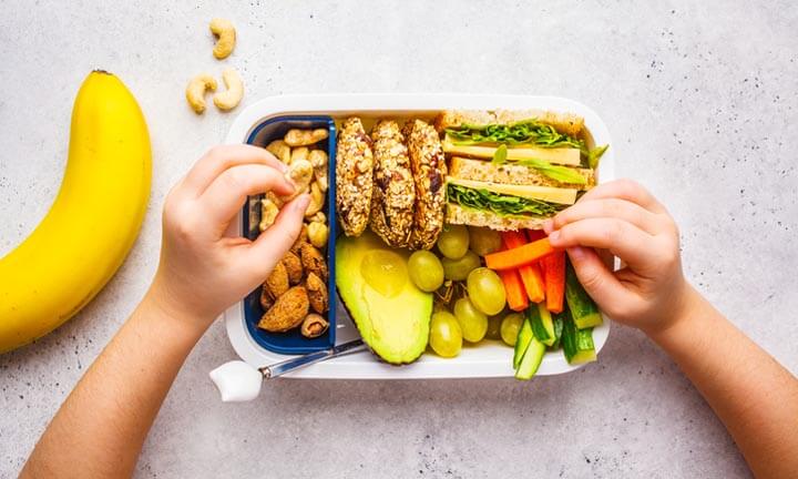 School healthy lunch box with sandwich, cookies, nuts, fruits and avocado on a white background.