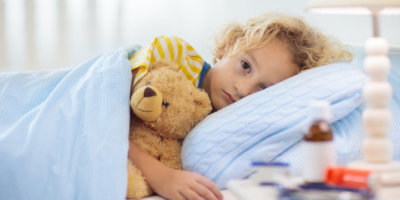 Kleines Kind liegt krank mit Teddy im Bett